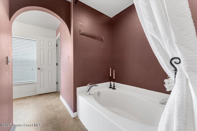 full bath with a textured ceiling, tile patterned flooring, a garden tub, and baseboards