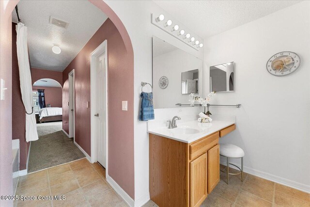 bathroom with a textured ceiling, vanity, visible vents, baseboards, and ensuite bath