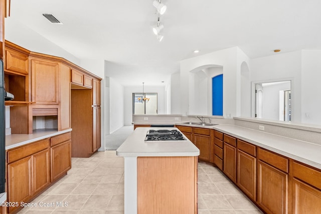 kitchen featuring light tile patterned flooring, stainless steel gas stovetop, sink, a center island, and an inviting chandelier