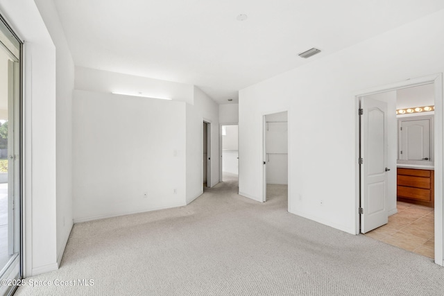 unfurnished bedroom featuring connected bathroom, a spacious closet, and light carpet