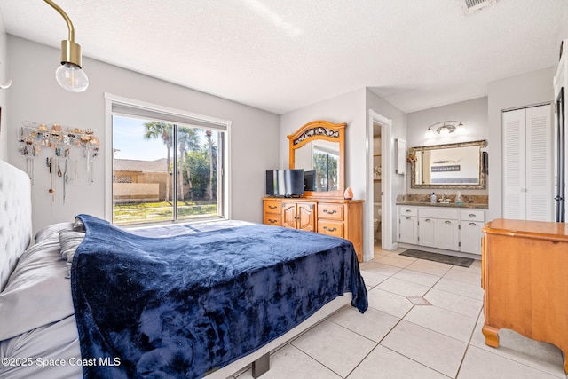 bedroom with connected bathroom, a textured ceiling, and light tile patterned flooring