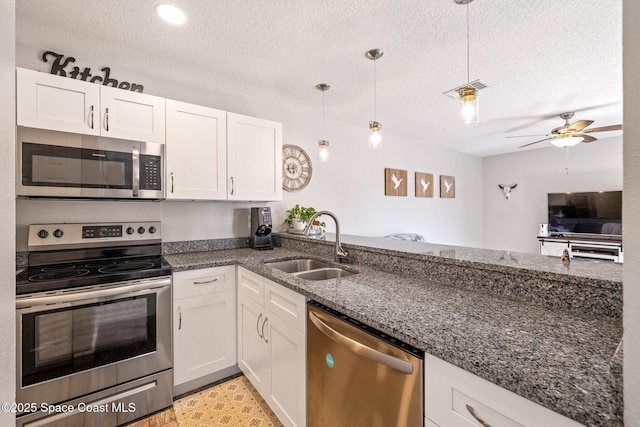 kitchen featuring sink, white cabinetry, dark stone counters, pendant lighting, and stainless steel appliances