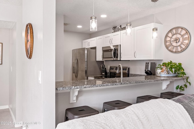 kitchen with appliances with stainless steel finishes, a breakfast bar, white cabinetry, hanging light fixtures, and kitchen peninsula