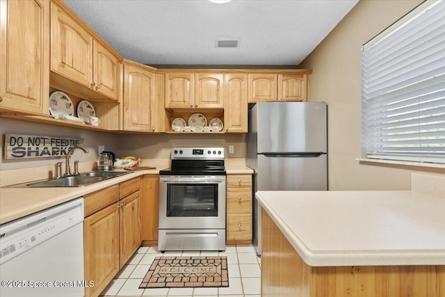 kitchen featuring light brown cabinetry, sink, a textured ceiling, light tile patterned floors, and stainless steel appliances