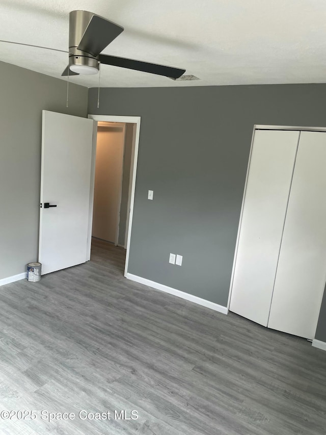 unfurnished bedroom with ceiling fan, a closet, wood finished floors, and baseboards