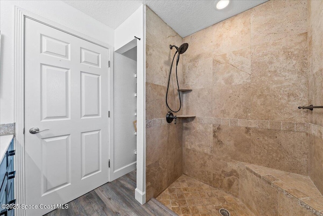 bathroom with a textured ceiling, wood-type flooring, and tiled shower