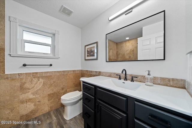 bathroom featuring toilet, tile walls, a textured ceiling, vanity, and hardwood / wood-style floors