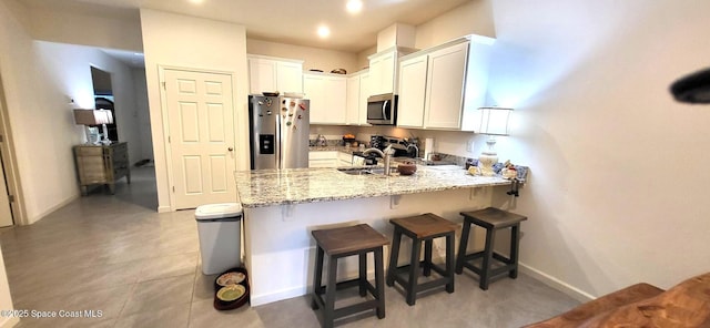 kitchen with a breakfast bar area, stainless steel appliances, light stone counters, white cabinets, and kitchen peninsula