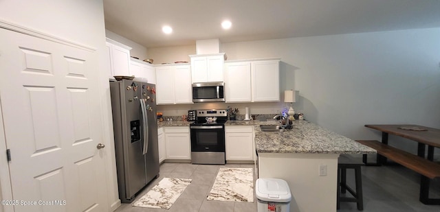 kitchen featuring white cabinetry, stainless steel appliances, light stone countertops, a kitchen bar, and kitchen peninsula