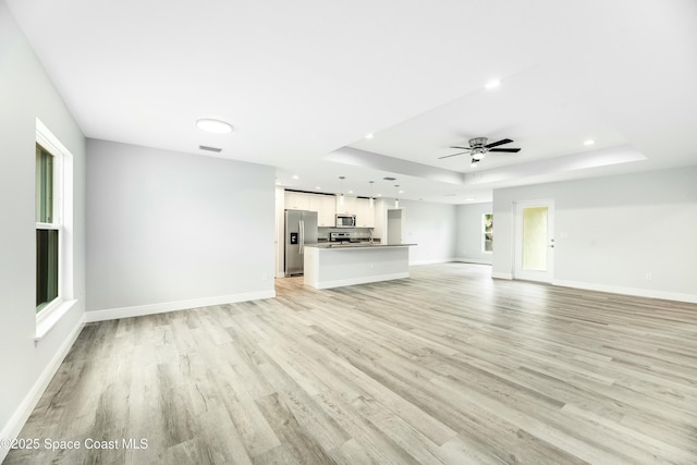 unfurnished living room featuring a raised ceiling, ceiling fan, and light wood-type flooring