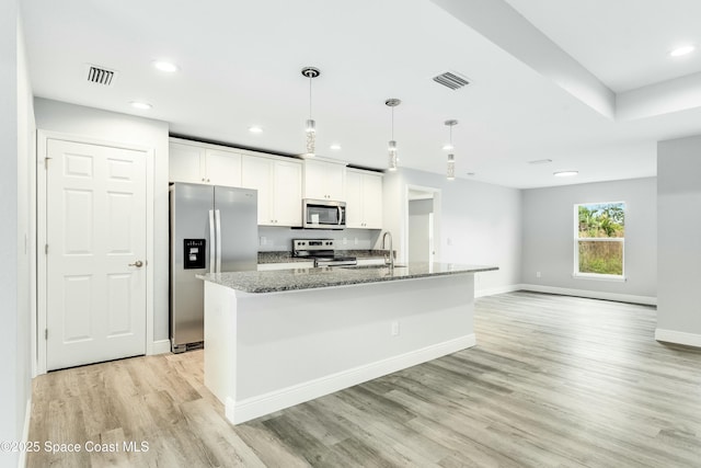 kitchen with stone countertops, white cabinetry, hanging light fixtures, stainless steel appliances, and a center island with sink