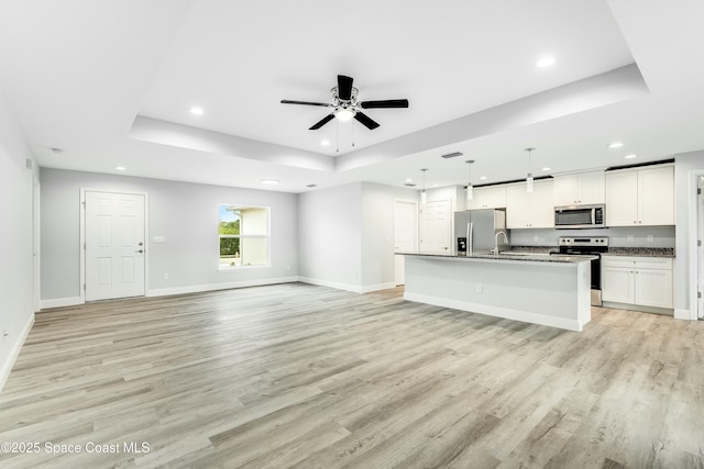 unfurnished living room with sink, a tray ceiling, ceiling fan, and light wood-type flooring