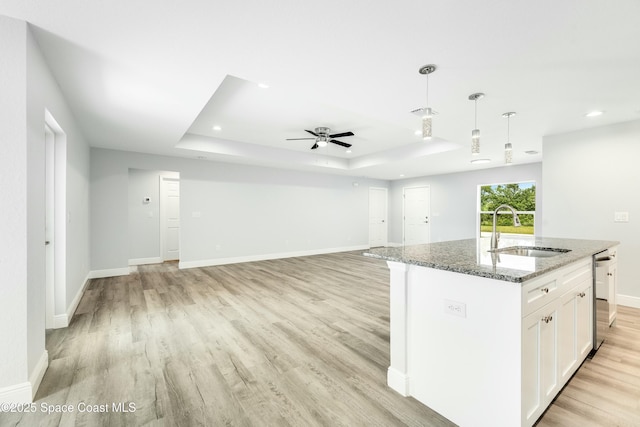 kitchen featuring sink, white cabinetry, dark stone countertops, a raised ceiling, and a kitchen island with sink