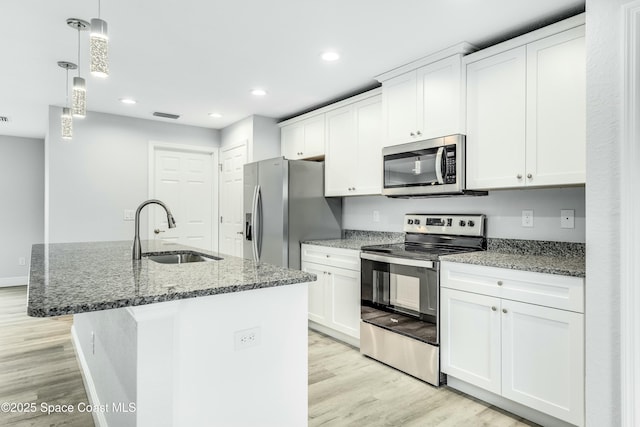 kitchen with sink, a kitchen island with sink, stainless steel appliances, white cabinets, and decorative light fixtures