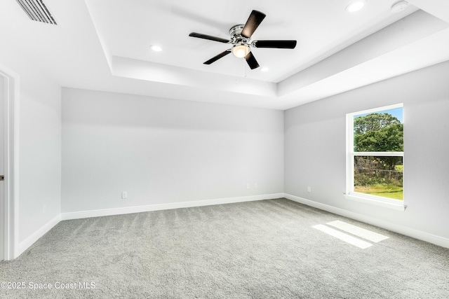 empty room featuring ceiling fan, carpet flooring, and a tray ceiling