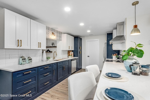 kitchen with sink, white cabinets, hanging light fixtures, blue cabinetry, and wall chimney exhaust hood