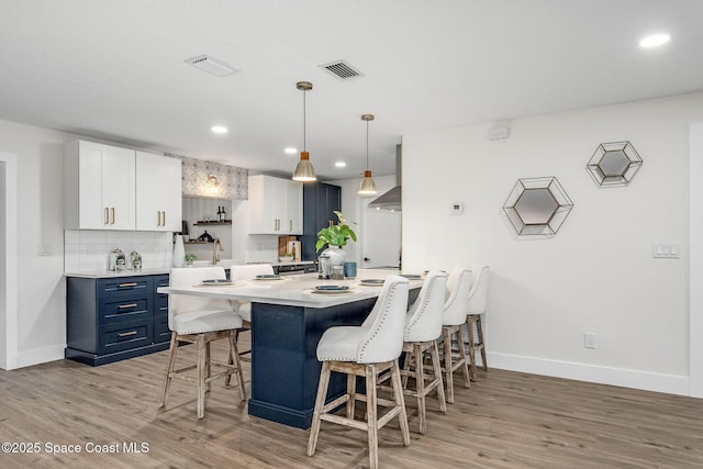 kitchen with blue cabinetry, white cabinetry, hanging light fixtures, a kitchen breakfast bar, and wall chimney exhaust hood