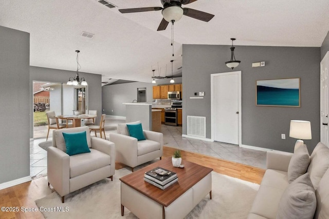 living room featuring ceiling fan with notable chandelier, light hardwood / wood-style floors, vaulted ceiling, and a textured ceiling