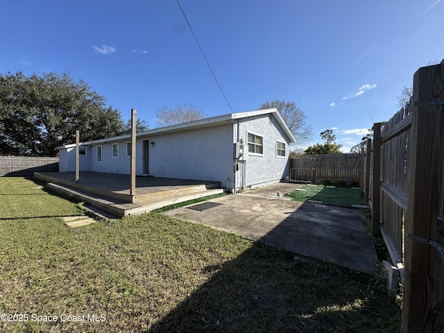 back of property featuring a wooden deck, a lawn, and a patio