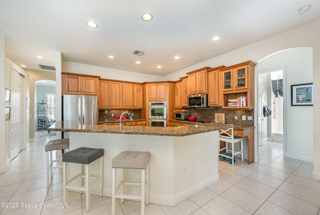 kitchen with stainless steel appliances, a kitchen bar, dark stone counters, and a spacious island