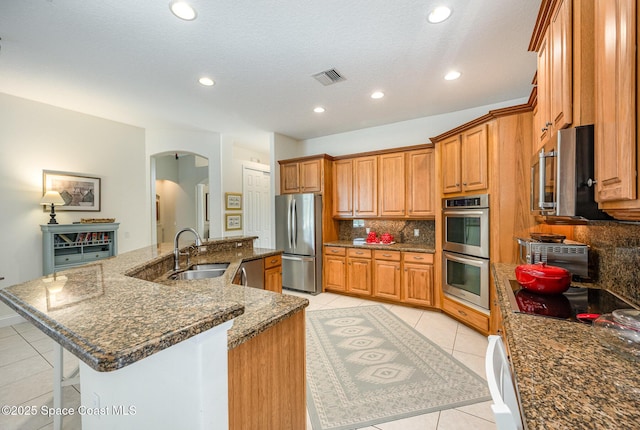 kitchen with a large island, sink, appliances with stainless steel finishes, dark stone countertops, and light tile patterned flooring