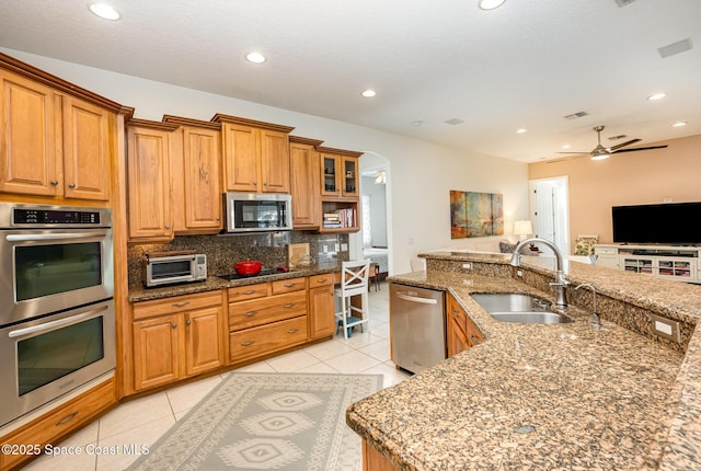 kitchen featuring sink, stone counters, appliances with stainless steel finishes, light tile patterned flooring, and decorative backsplash