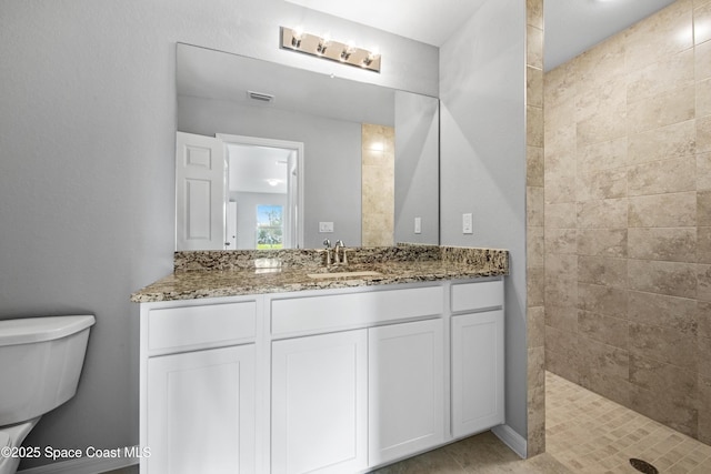 bathroom with vanity, tiled shower, and toilet