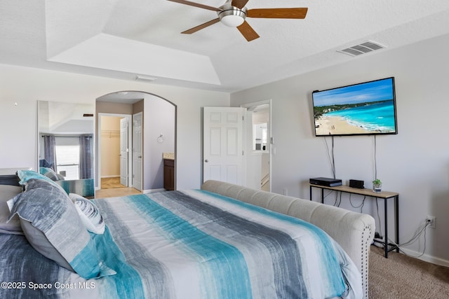 bedroom featuring a spacious closet, light carpet, a textured ceiling, a tray ceiling, and ceiling fan