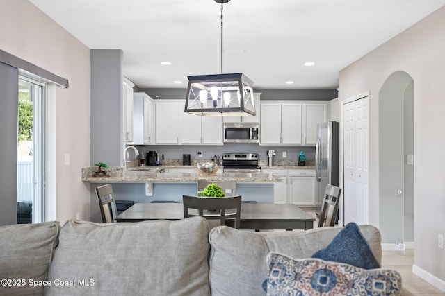 kitchen with appliances with stainless steel finishes, pendant lighting, white cabinetry, sink, and light stone countertops