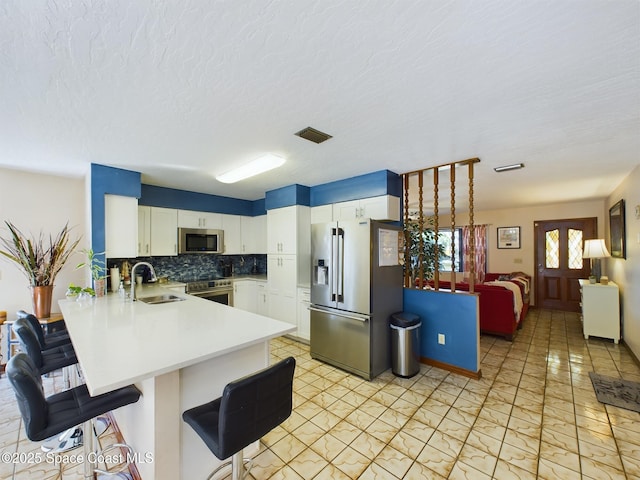 kitchen featuring sink, appliances with stainless steel finishes, kitchen peninsula, white cabinets, and backsplash