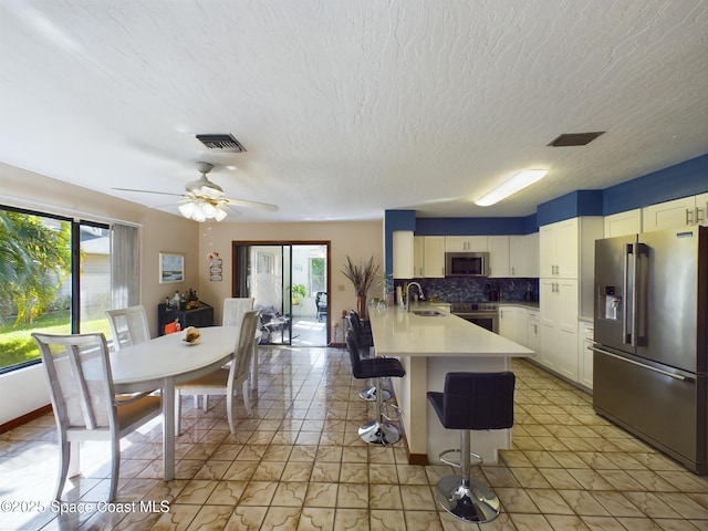 kitchen featuring sink, appliances with stainless steel finishes, a kitchen breakfast bar, white cabinets, and decorative backsplash