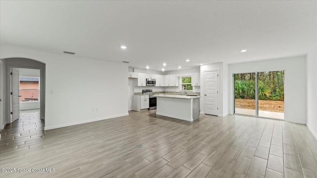 kitchen featuring visible vents, white cabinets, arched walkways, open floor plan, and stainless steel appliances