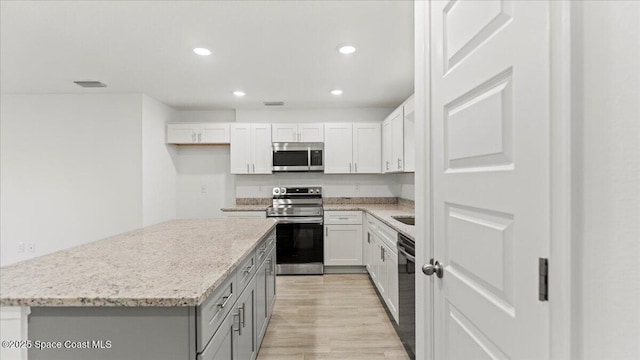 kitchen with light stone counters, stainless steel appliances, visible vents, gray cabinetry, and a kitchen island