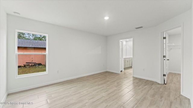 empty room with light wood-type flooring, visible vents, and baseboards