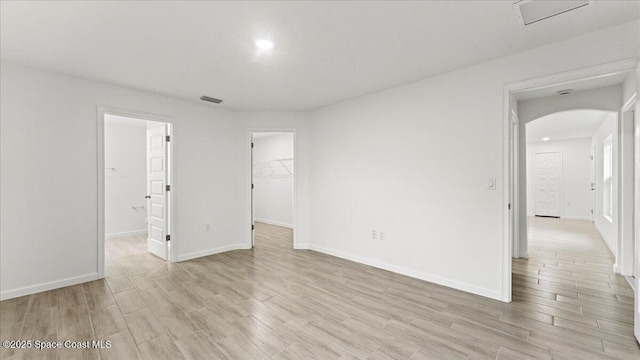 unfurnished room featuring arched walkways, light wood-type flooring, visible vents, and baseboards