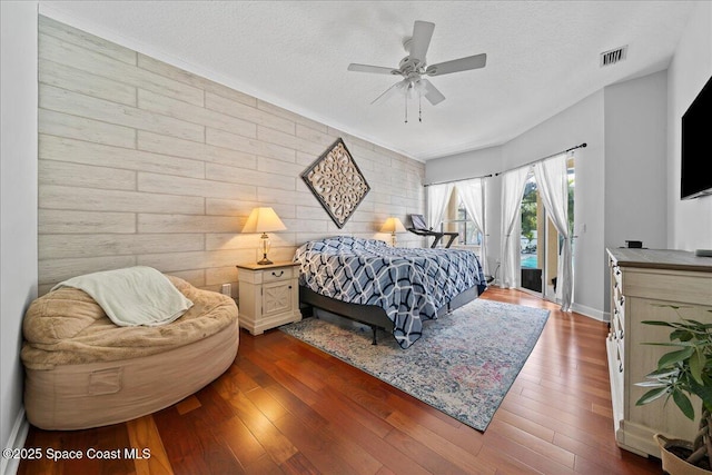 bedroom with ceiling fan, dark hardwood / wood-style floors, access to outside, and a textured ceiling