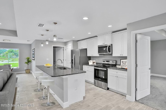 kitchen featuring dark stone countertops, white cabinetry, stainless steel appliances, and a center island with sink