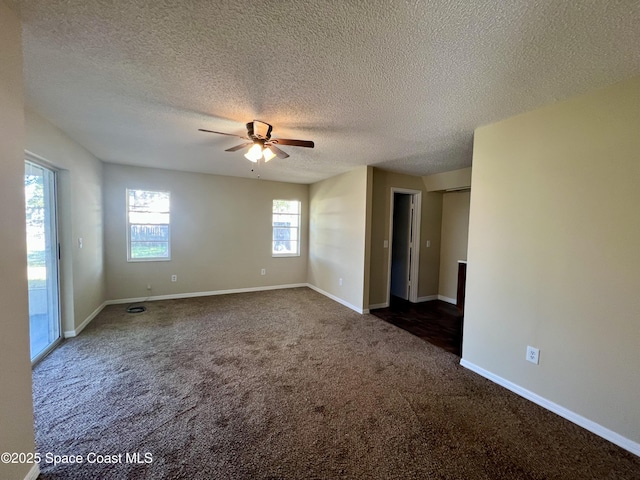 spare room with ceiling fan, a textured ceiling, and dark carpet