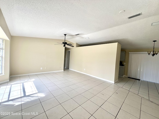 tiled empty room featuring lofted ceiling, ceiling fan with notable chandelier, and a textured ceiling