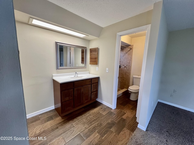 bathroom with toilet, a textured ceiling, a tile shower, vanity, and hardwood / wood-style flooring