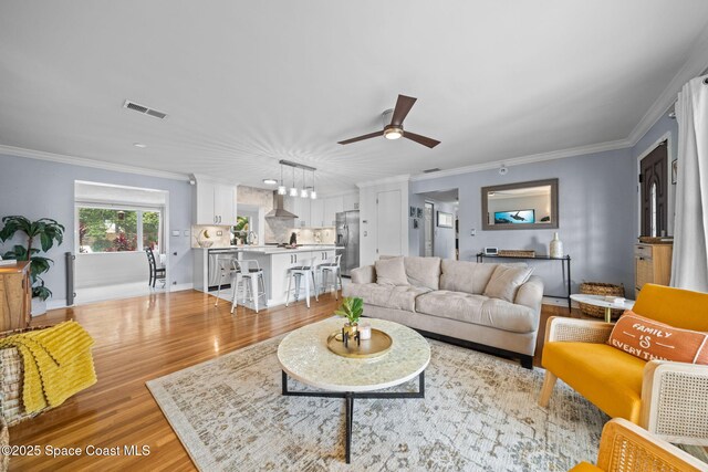 living room with crown molding, ceiling fan, and light wood-type flooring