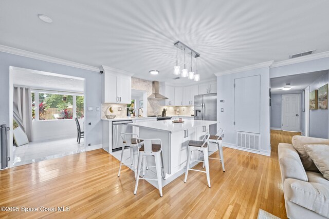 kitchen featuring appliances with stainless steel finishes, decorative light fixtures, white cabinets, a kitchen bar, and wall chimney range hood