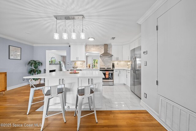 kitchen with appliances with stainless steel finishes, a breakfast bar area, white cabinets, and wall chimney exhaust hood