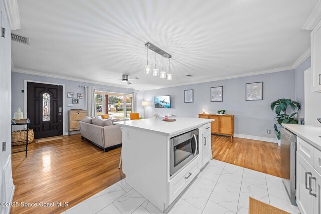 kitchen featuring crown molding, appliances with stainless steel finishes, white cabinetry, hanging light fixtures, and a kitchen island