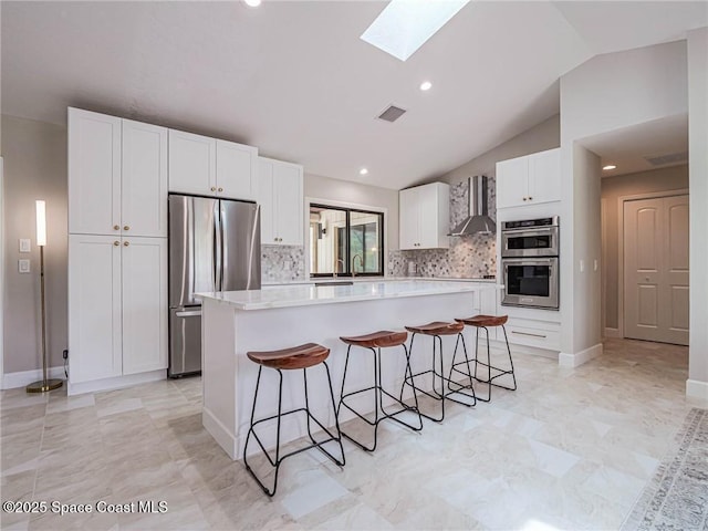 kitchen featuring a kitchen island, a breakfast bar area, white cabinets, stainless steel appliances, and wall chimney range hood