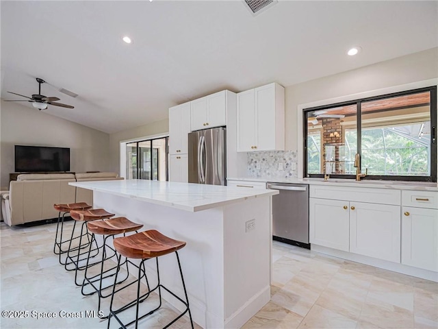 kitchen featuring sink, white cabinetry, stainless steel appliances, light stone countertops, and a kitchen island