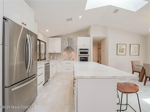 kitchen featuring sink, white cabinetry, a center island, appliances with stainless steel finishes, and wall chimney range hood