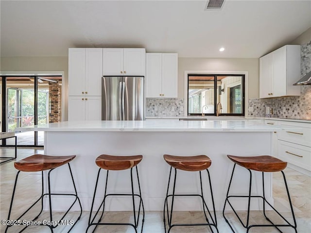 kitchen with white cabinetry, plenty of natural light, a center island, and stainless steel fridge