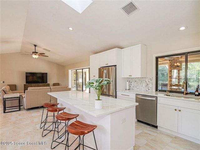 kitchen featuring sink, white cabinetry, stainless steel appliances, a center island, and a kitchen bar