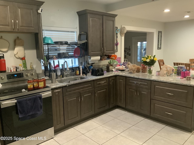 kitchen with light tile patterned floors, light stone counters, a sink, dark brown cabinets, and stainless steel range with electric stovetop